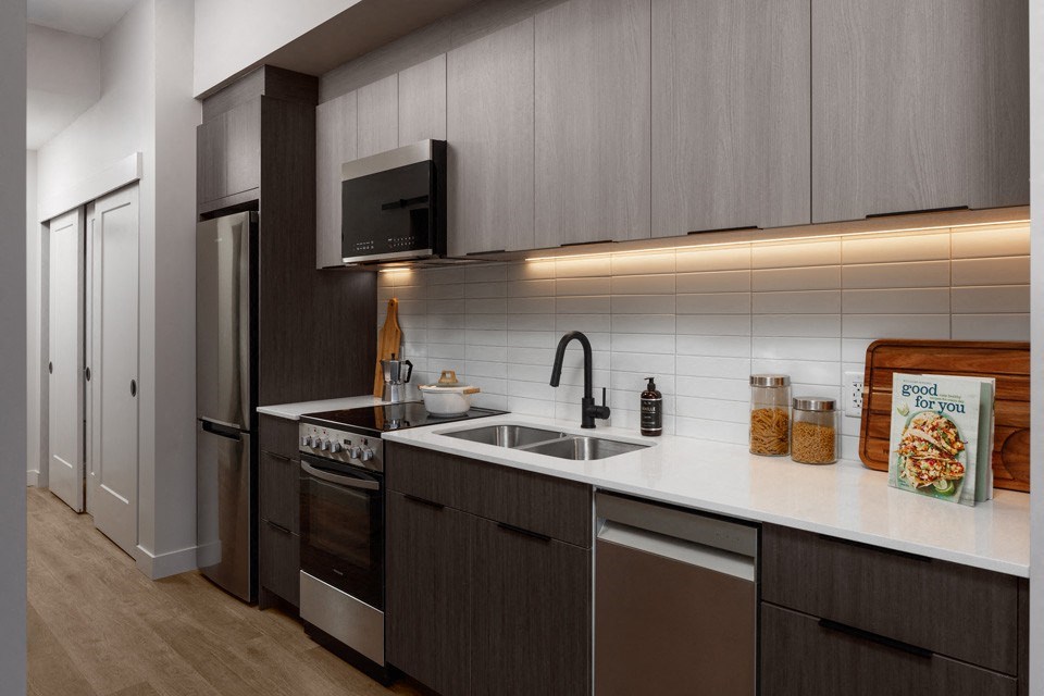 A modern kitchen with dark wood cabinets and stainless steel appliances at The Ambrosi in Kelowna, BC.