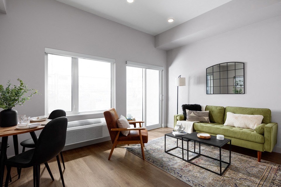 A living room with a green couch, a wooden table, and a rug at The Ambrosi in Kelowna, BC.
