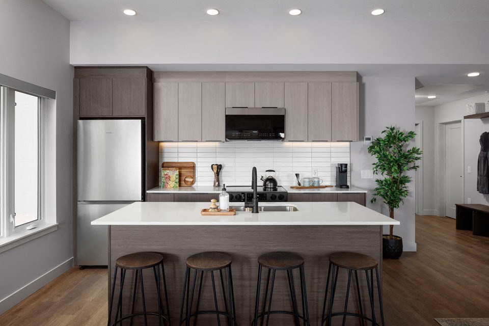 A modern kitchen with a white island and bar stools at The Ambrosi in Kelowna, BC.