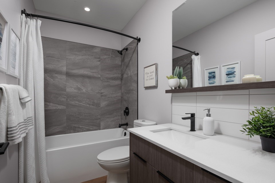 A modern bathroom with a white toilet, a white sink, and a grey shower at The Ambrosi in Kelowna, BC.