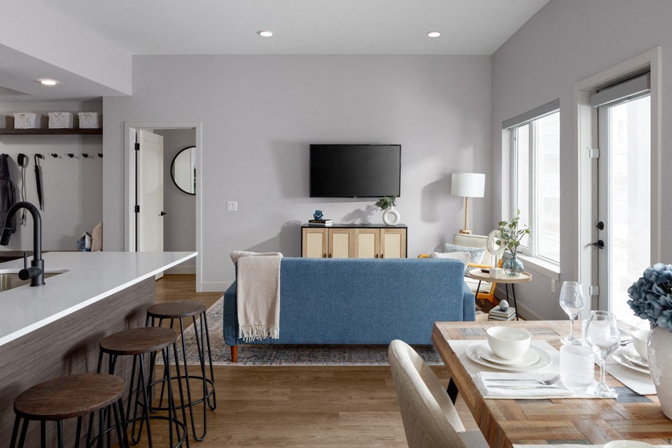 A modern kitchen with a blue sofa in the living room at The Ambrosi in Kelowna, BC.