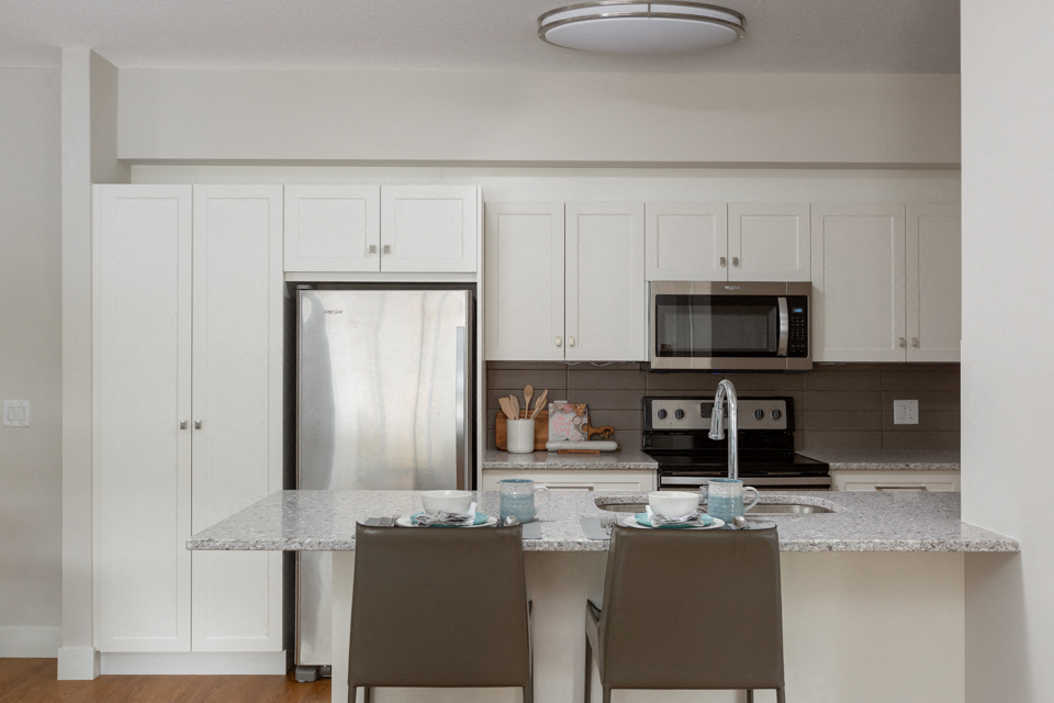 The Conservatory stunning kitchen with white cabinetry and built-in breakfast bar in Kelowna, BC