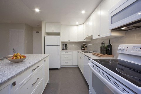 A kitchen with white cabinets and appliances, a bowl of fruit on the counter, and a wine bottle on the counter.