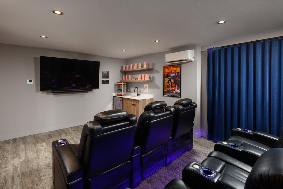 A theatre room with black leather chairs and a flat screen TV at The Ambrosi in Kelowna, BC.