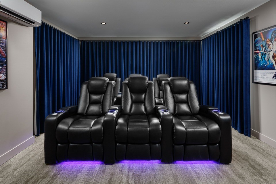 A theatre room with a row of black leather recliner chairs with blue curtains at The Ambrosi in Kelowna, BC.