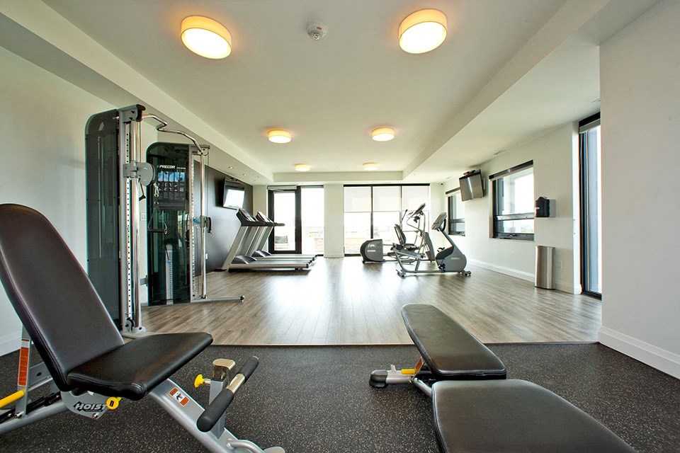 Gym with exercise equipment and windows, located in Building B at Trio on Belmont in Kitchener, ON