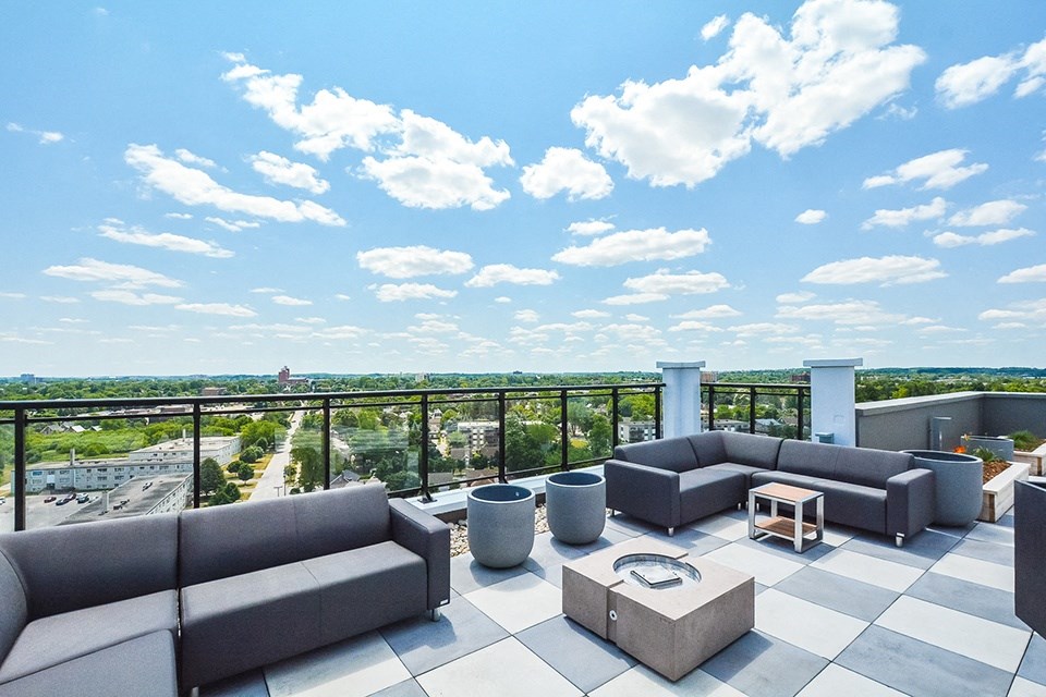 A rooftop patio with outdoor padded sectional couches and a view of the city at Trio on Belmont in Kitchener, ON