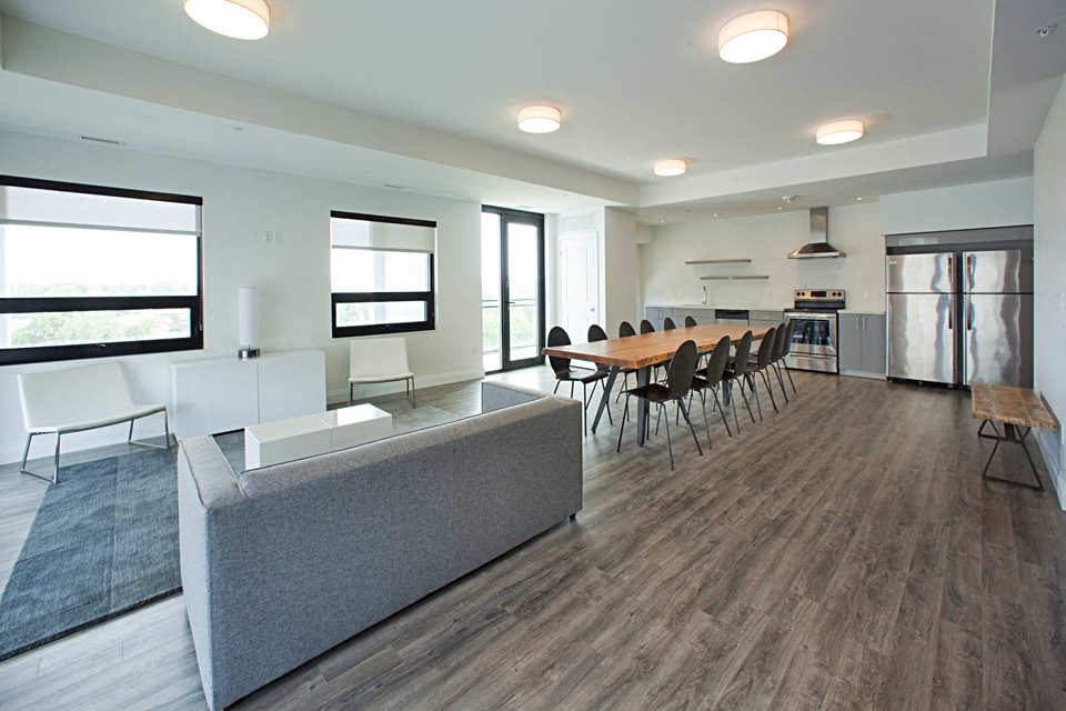 Trio on Belmont large social room with couch seating area, long table with chairs, and kitchen in Kitchener, ON