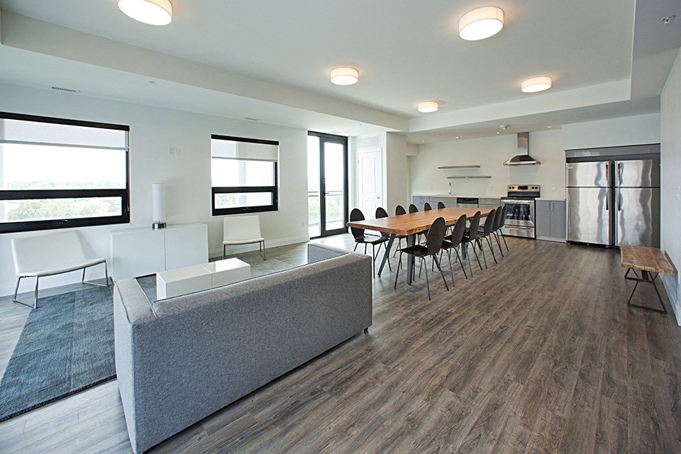Social room with lounge area, large dining table and chairs and full kitchen located in Building C at Trio on Belmont in Kitchener, ON