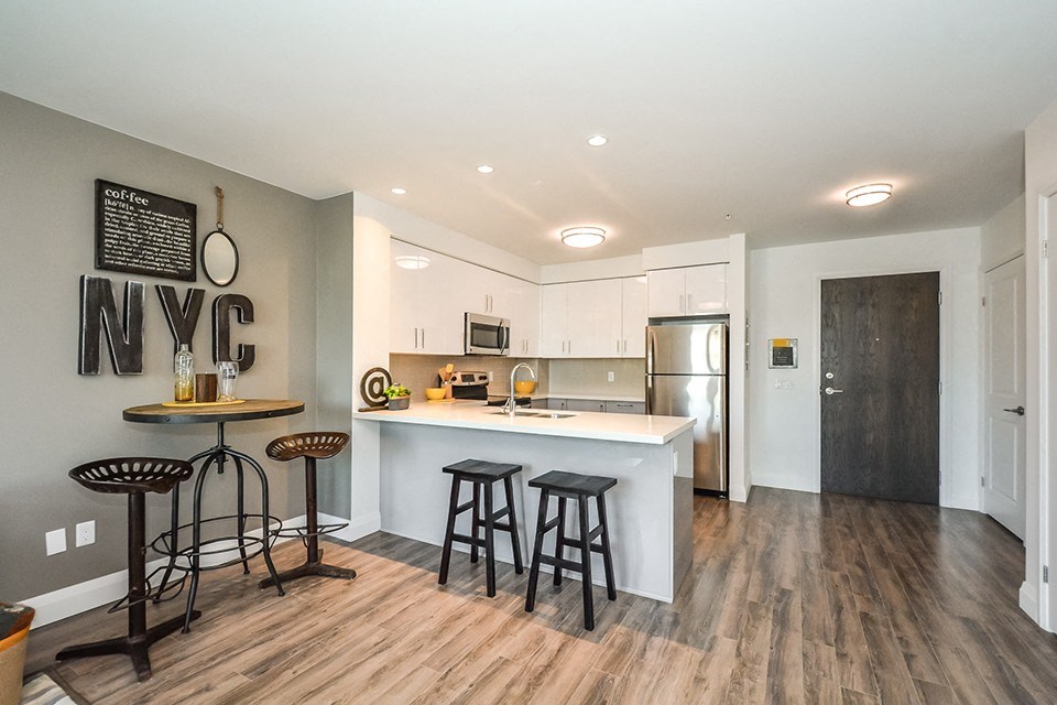 Two bars at a breakfast bar in an open-concept kitchen, with a dinette to the left, in a 1 bed 1 bath variation B in building A at Trio on Belmont in Kitchener, ON