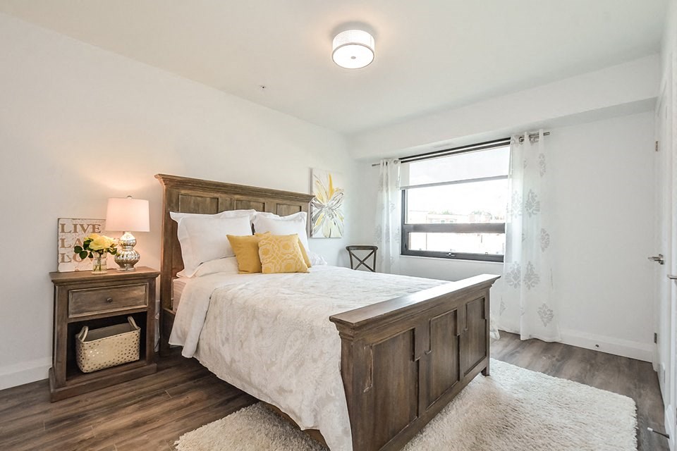 2nd bedroom with a large bed with wooden frame and window in a 2 bed + den 2 bath variation E in building A at Trio on Belmont in Kitchener, ON