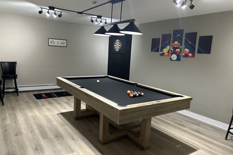 A pool table with a black felt cloth and a light hanging above it.