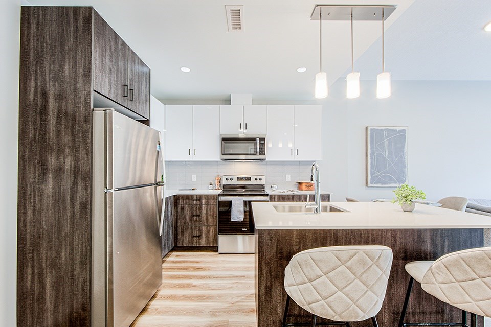 View of a kitchen with wood-look lower and white upper cabinets and a kitchen island with two bar stools in a 2 bedroom 2 bathroom variation C layout at Vale Station Apartments in Waterloo, Ontario