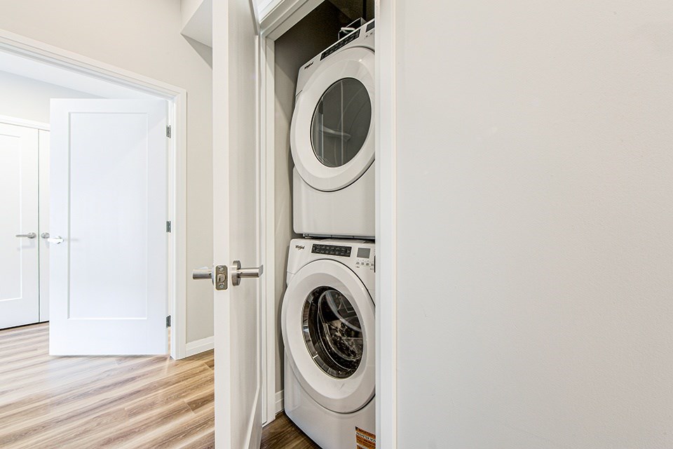 Laundry closet with stacked white washer and dryer in a 2 bedroom 2 bathroom variation C layout at Vale Station Apartments in Waterloo, Ontario