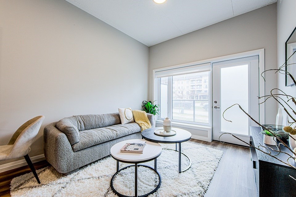 A living room with a grey couch, two round coffee tables, large window and door to a patio in a 2 bedroom 2 bathroom variation C layout at Vale Station Apartments in Waterloo, Ontario