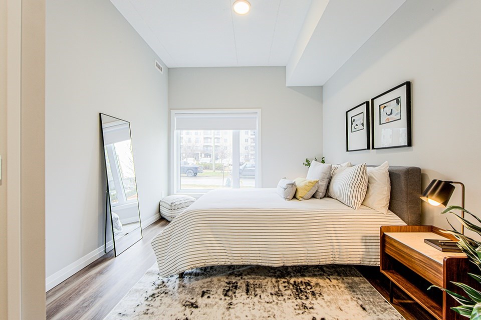 Primary bedroom with a large bed, bedside table and floor standing mirror in a 2 bedroom 2 bathroom variation C layout at Vale Station Apartments in Waterloo, Ontario