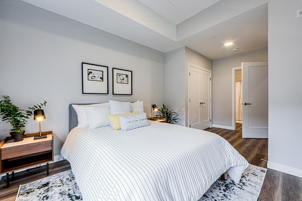 Primary bedroom with a large bed, bedside tables and two framed pictures on the wall in a 2 bedroom 2 bathroom variation C layout at Vale Station Apartments in Waterloo, Ontario