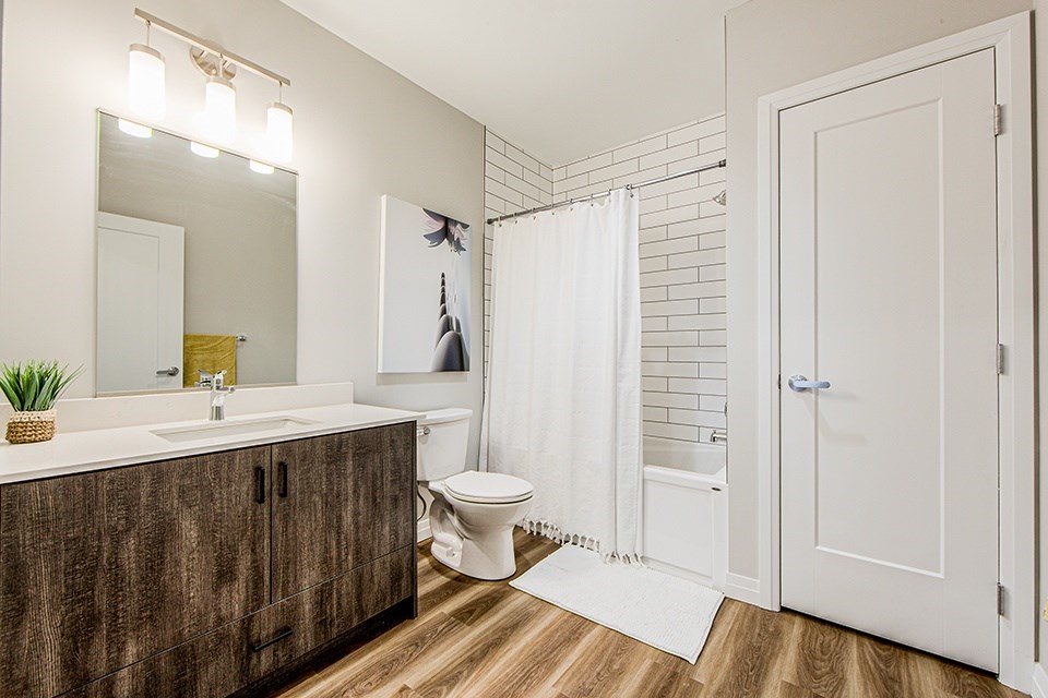 Ensuite bathroom with a large soaker tub with a tiled surround, large vanity, white toilet and linen closet at Vale Station Apartments in Waterloo, Ontario