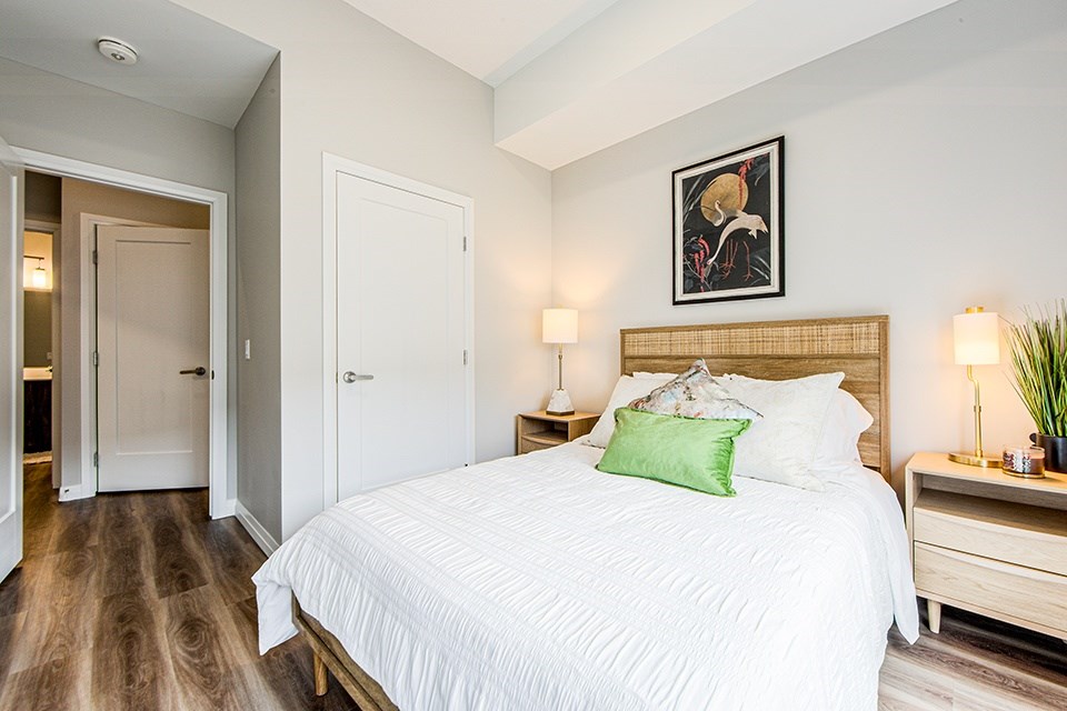 Second bedroom with a large bed and a painting above it in a 2 bedroom 2 bathroom variation C layout at Vale Station Apartments in Waterloo, Ontario