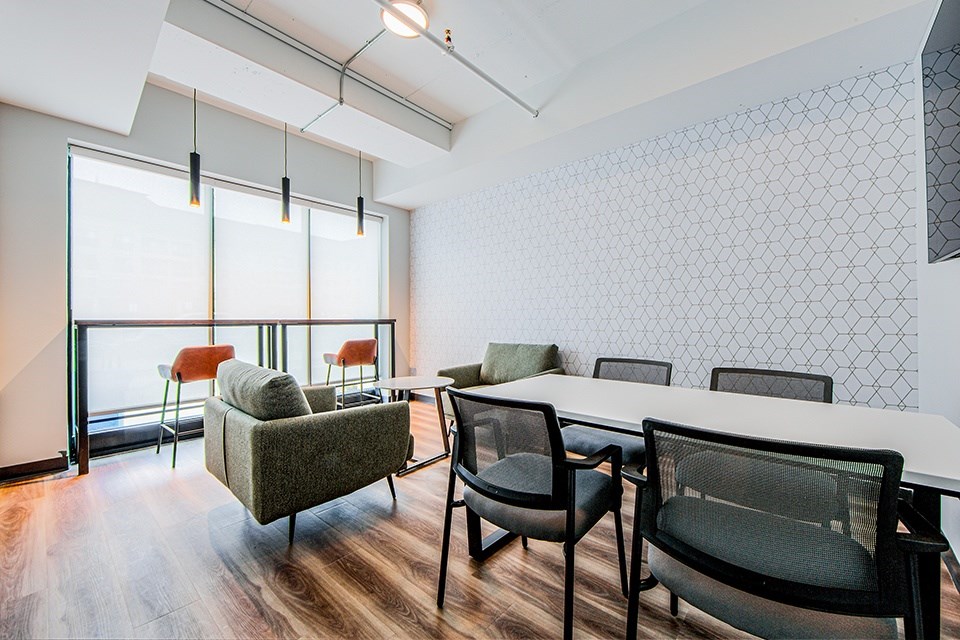 Shared workspace with a conference table, soft club chairs and bar-height counter with two stools looking out a large window at Vale Station Apartments in Waterloo, Ontario