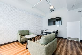 Shared workspace with soft club chairs, conference table with four chairs and a flat screen TV at Vale Station Apartments in Waterloo, ON