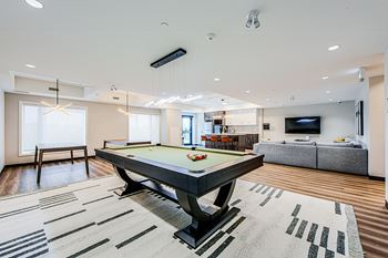 Social room with a pool table with TV lounge area and kitchen seen in the background at Vale Station Apartments in Waterloo, Ontarion