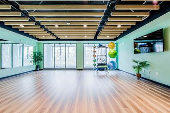 Yoga and Pilates studio with wooden floors and a green walls, large window and wood slat ceiling. Flat screen TV mounted on the wall and stretching equipment at Vale Station Apartments in Waterloo, Ontario