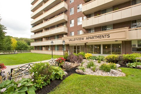 Exterior entrance of Valleyview Apartments with wooden benches and healthy flowerbeds