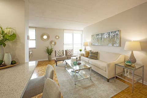 A living room with a white couch, a glass coffee table, and a large painting on the wall.