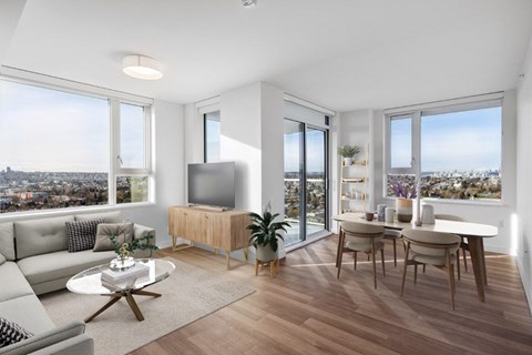 A modern living room with a grey sofa, a wooden cabinet, a glass table, and a view of the city.