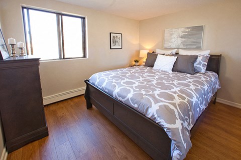 Mountain View Bedroom with window on the left. A big soft bed is in the middle of the room, with a painting hung above the headboard and a lamp on a nightstand beside it in Collingwood, ON