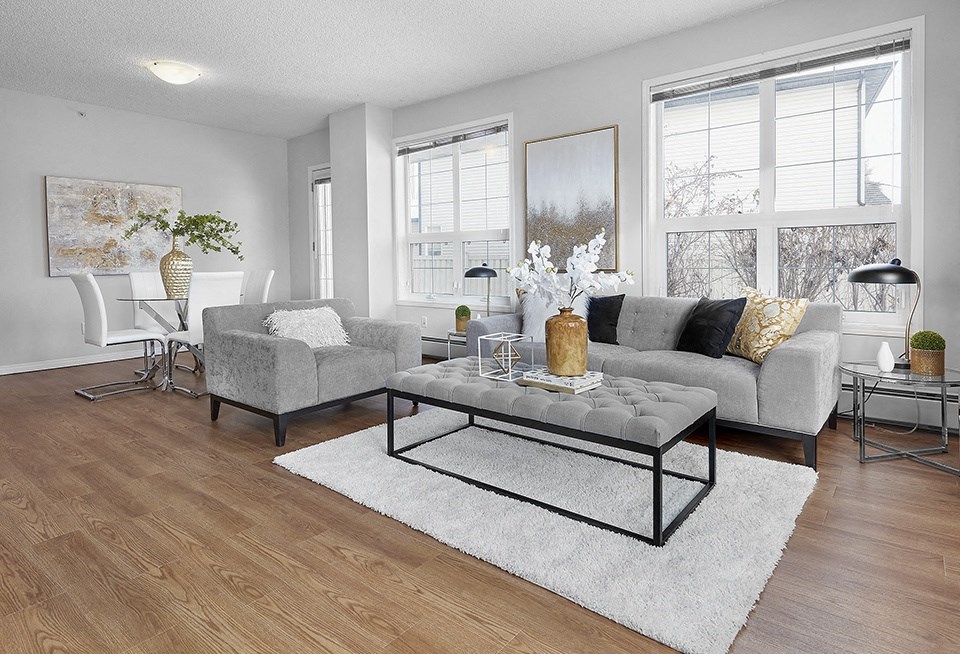 A modern living room with a grey sofa, a glass coffee table, and a white chair.