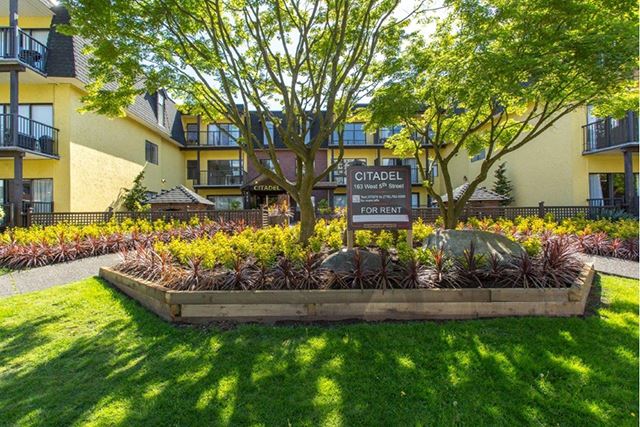 Take in modern, high end architecture Citadel in North Vancouver, BC Building exterior with vibrant flowerbeds full of greenery and trees