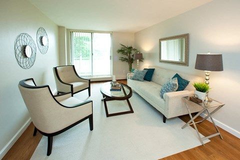A living room with a white couch, two chairs, and a small table with a lamp and a plant.