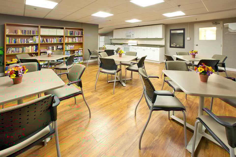 Lord Simcoe Apartments social room with tables and chairs, bookshelf filled with books, and