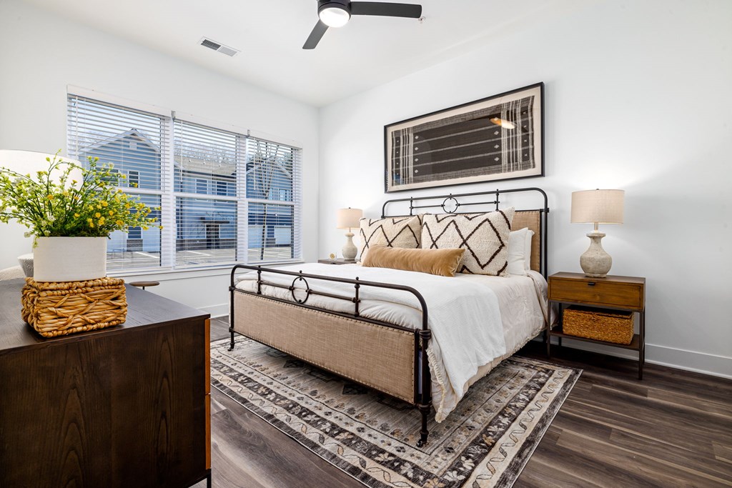 A bedroom with a large bed, a wooden nightstand, and a plant on a table.