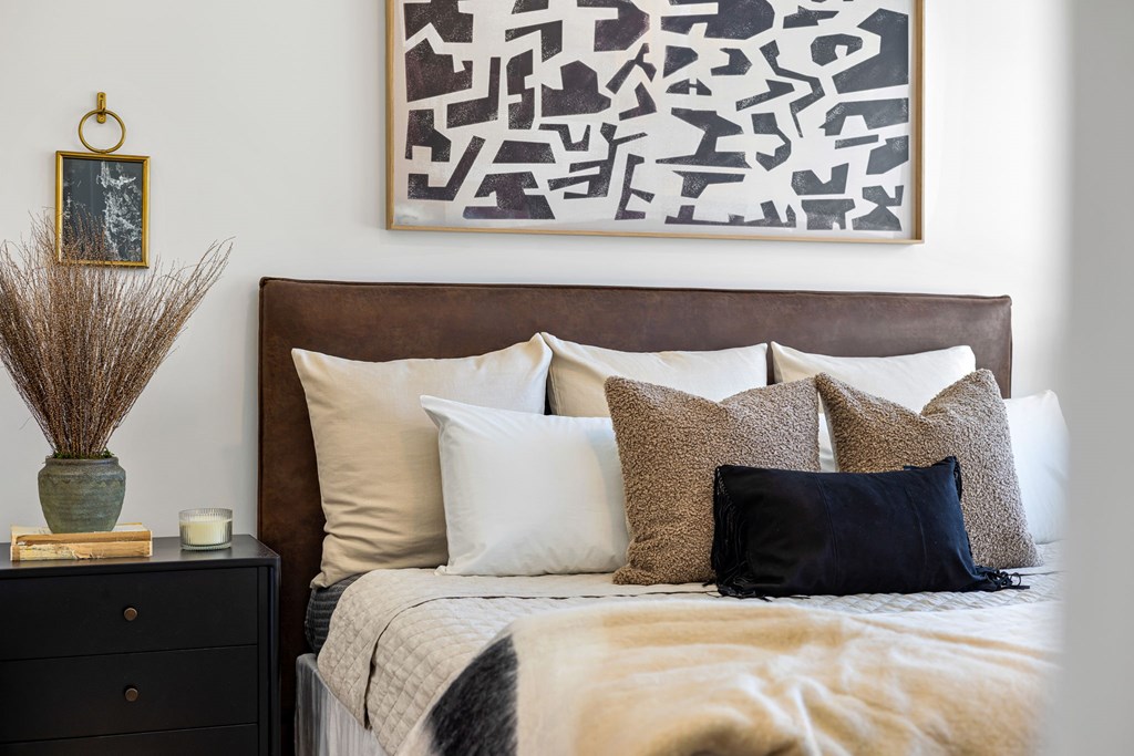 A bed with a brown headboard and a large abstract painting above it.