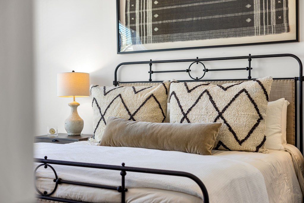 A bed with a black metal frame and a white comforter with a patterned pillow.