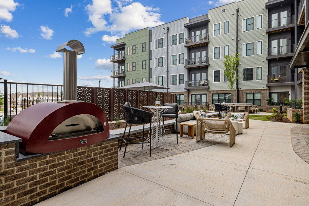 A brick oven is on a patio with chairs and a table.