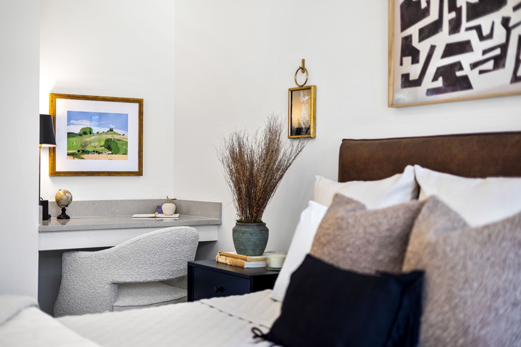 A bedroom with a bed, desk, chair, and a painting on the wall.