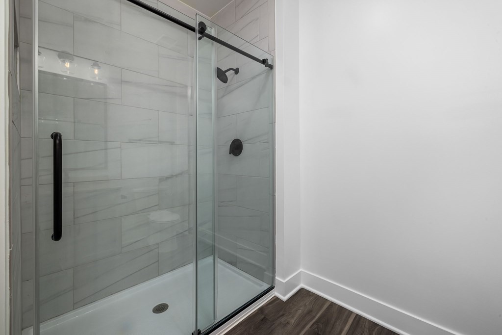 A glass shower stall with a black handle and a black pipe.
