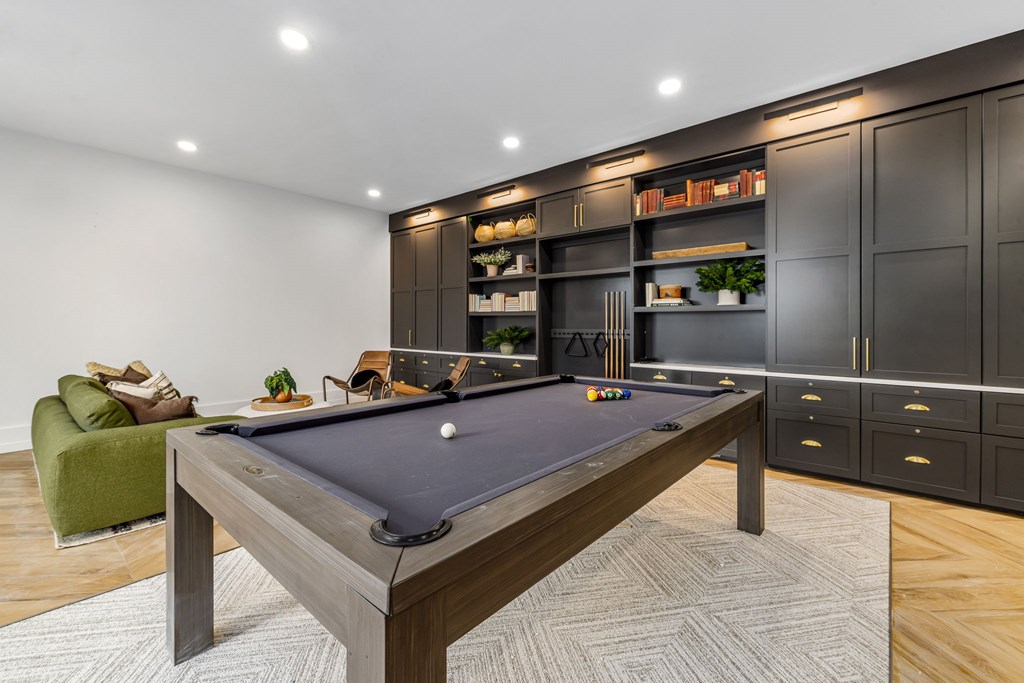 A pool table is in the middle of a room with a green chair and a cabinet with shelves.