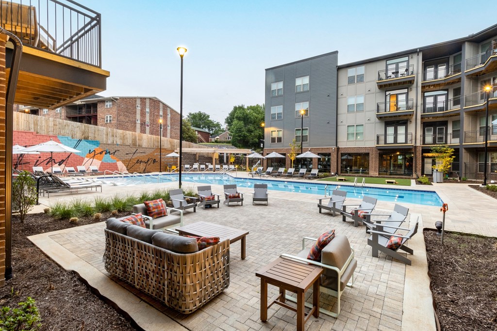 a swimming pool with lounge chairs and tables in front of an apartment building