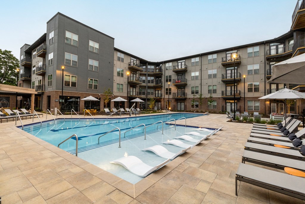 a swimming pool with lounge chairs in front of an apartment building