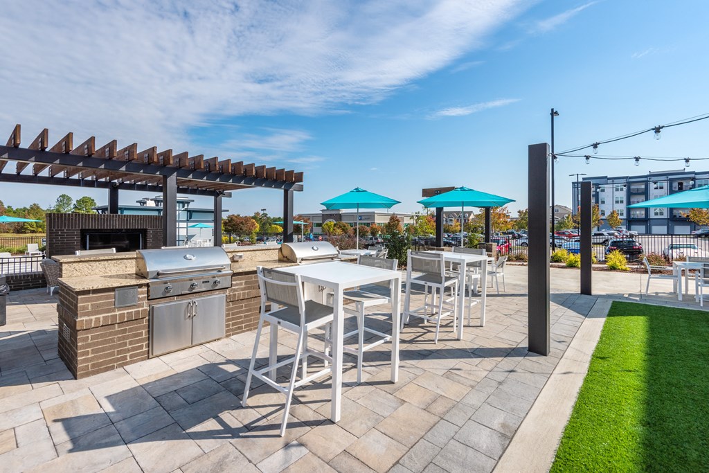 a patio with a grill and tables with chairs and umbrellas