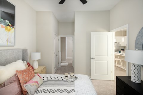 A bedroom with a bed, a painting, a ceiling fan, and a door leading to another room.