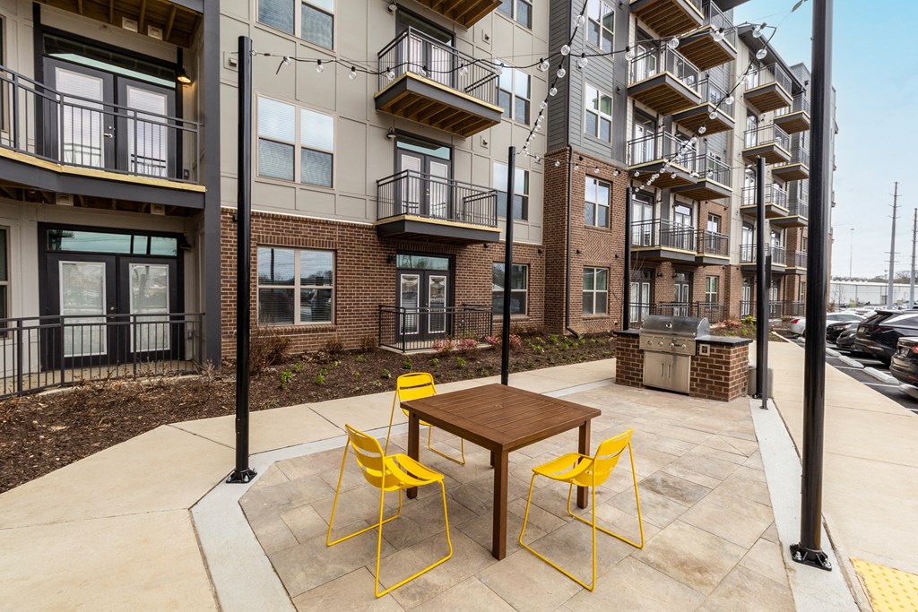 a patio with a table and yellow chairs in front of an apartment building
