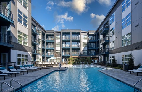 A swimming pool in front of a building with lounge chairs around it.