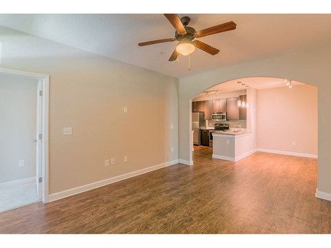 an empty living room with a ceiling fan and a kitchen