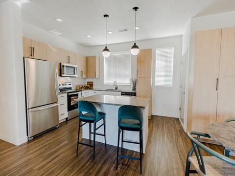 a kitchen with an island with blue chairs and a stainless steel refrigerator